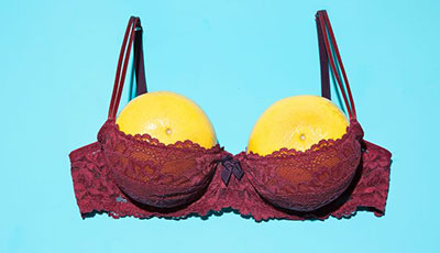 Two lumpy yellow lemons placed inside a bra with a blue background