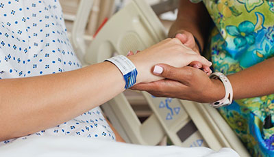 Patient with hospital identification bracelet holding the hand of their nurse while in their hospital bed