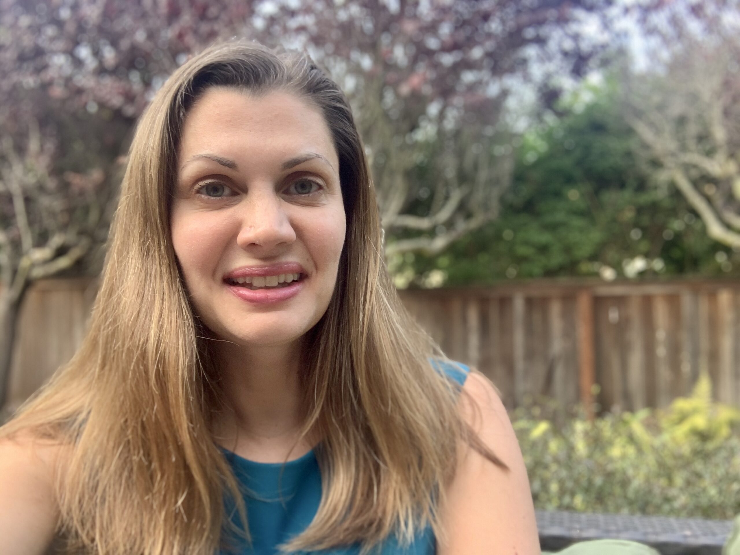 Anne Peled smiling outside wearing a green shirt with plants in the background